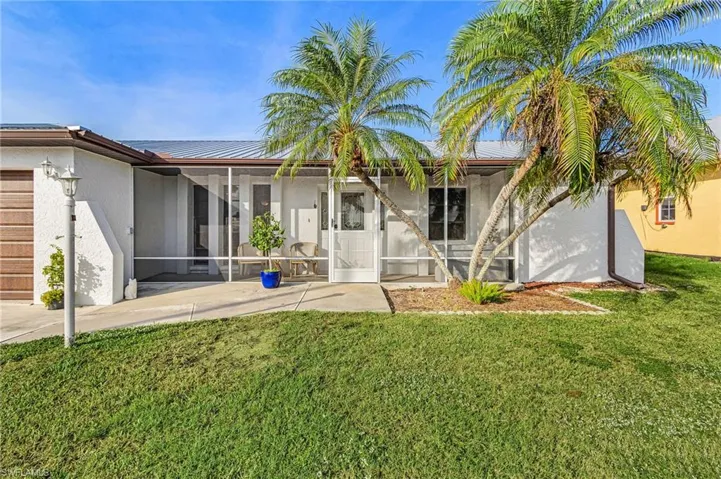 Front view of property featuring a lawn, stucco siding, a screened porch, and a metal roof
