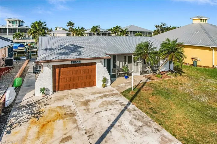 View of front of house featuring a metal roof, concrete driveway, a front yard, a sunroom, and stucco siding