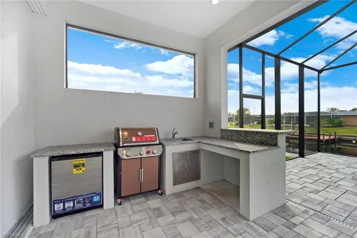 Outdoor kitchen with Weber grill, stainless steel refrigerator, sink and bar