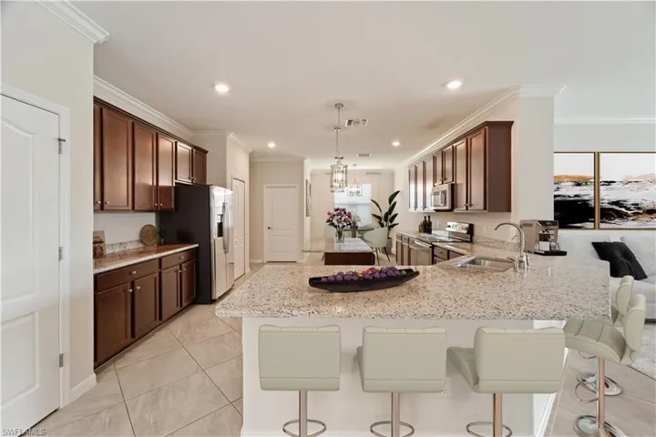 Virtually Staged Kitchen with stainless steel appliances, light stone counters, crown molding, sink, and light tile patterned floors.