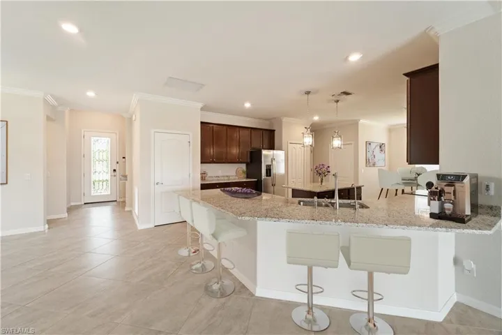 Virtually Staged Kitchen with stainless steel appliances, light stone counters, crown molding, sink, and light tile patterned floors.