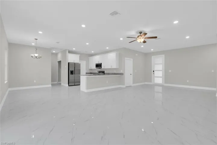 Open-concept living space featuring expansive light-toned tile flooring, recessed ceiling lighting, and a kitchen with white cabinetry