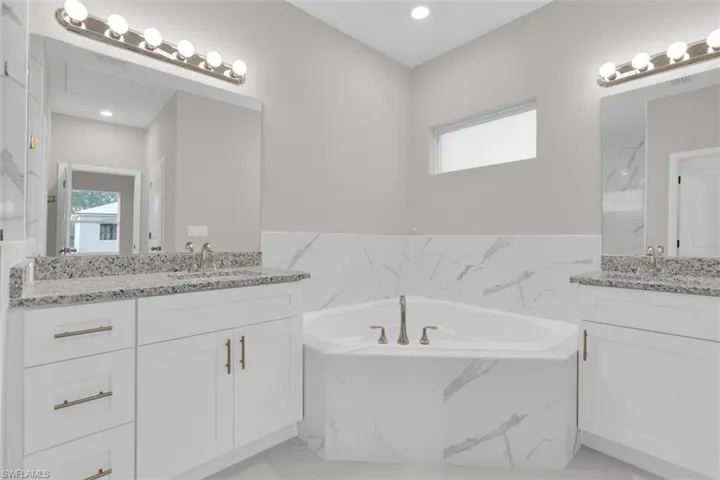 Corner soaking tub with a tiled surround, flanked by twin vanity cabinets featuring granite countertops and undermount sinks