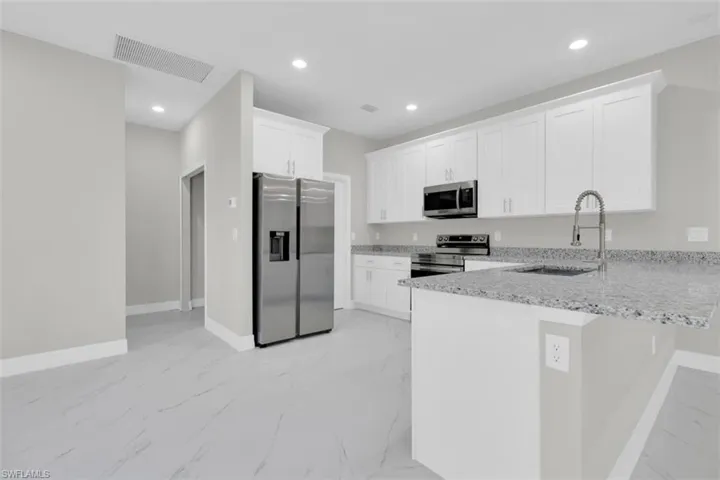 Kitchen featuring white shaker-style cabinetry, stainless steel appliances, granite countertops, and light gray tile flooring