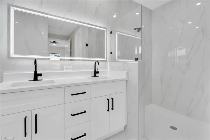 Contemporary bathroom featuring a double vanity with integrated sinks, matte black hardware, an illuminated mirror, and a glass-enclosed shower with a built-in bench