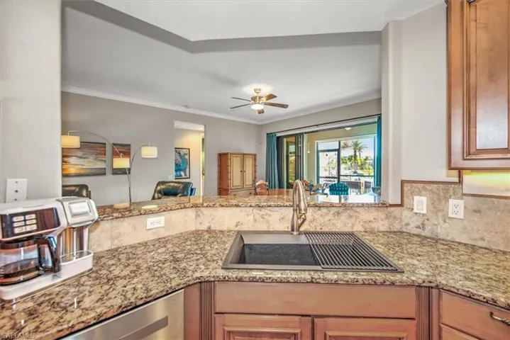 Kitchen with light stone countertops, stainless steel dishwasher, ornamental molding, ceiling fan, and sink