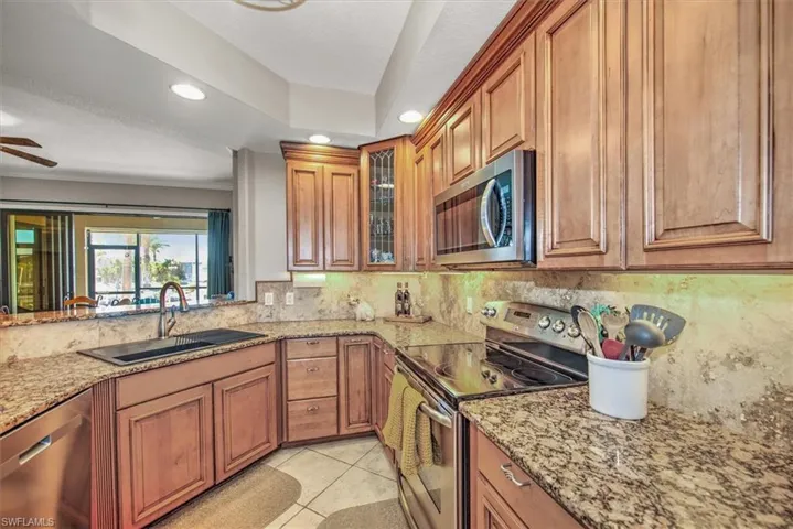 Kitchen with sink, light stone counters, light tile patterned floors, decorative backsplash, and appliances with stainless steel finishes