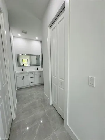 Full bathroom with double vanity, a closet, light marble finish floors, and recessed lighting