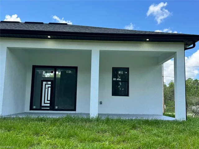 View of exterior entry with stucco siding, covered porch, and a shingled roof