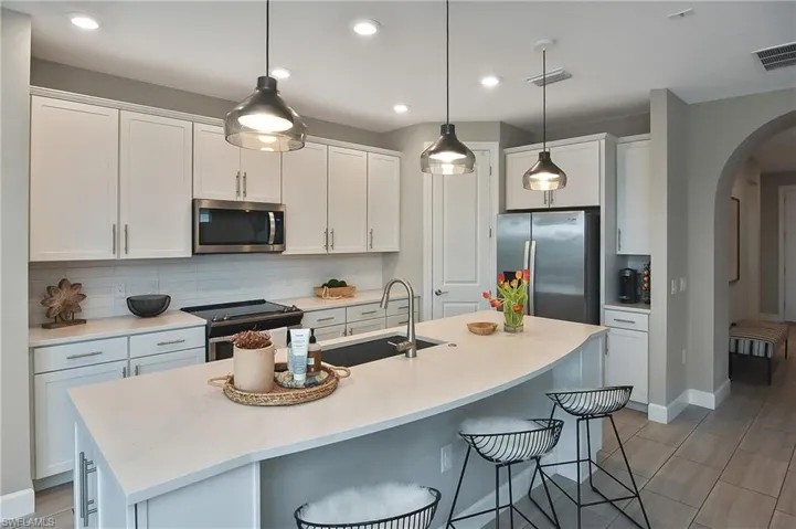 Kitchen with appliances with stainless steel finishes, a breakfast bar, white cabinetry, and an island with sink