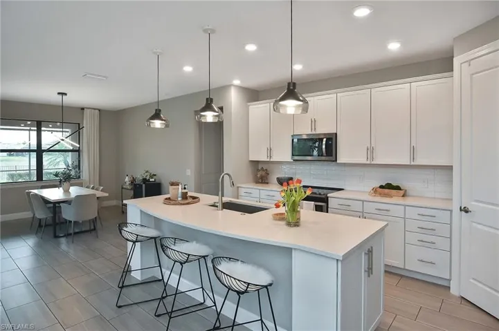 Kitchen featuring a center island with sink, sink, white cabinetry, stainless steel appliances, and hanging light fixtures