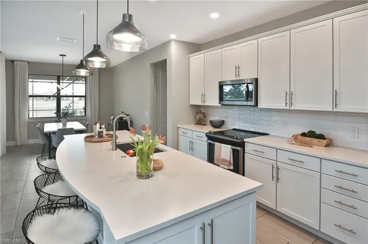 Kitchen featuring sink, white cabinetry, pendant lighting, stainless steel appliances, and a kitchen island with sink