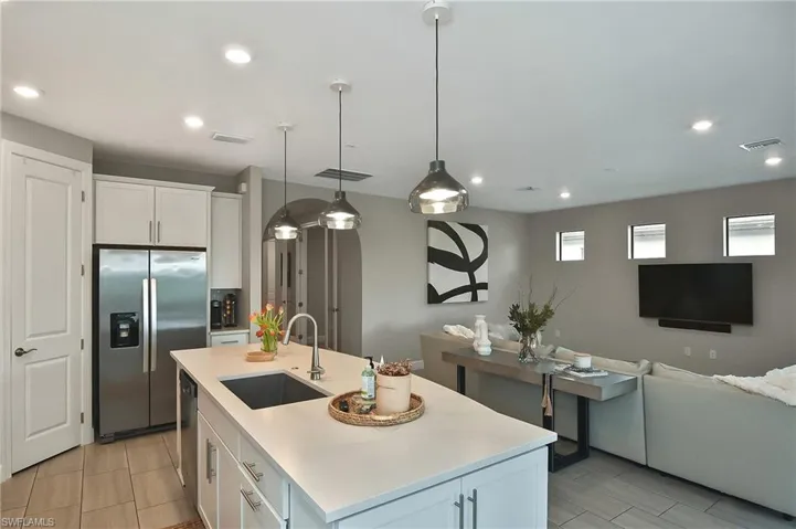 Kitchen featuring a center island with sink, decorative light fixtures, stainless steel fridge, sink, and white cabinetry