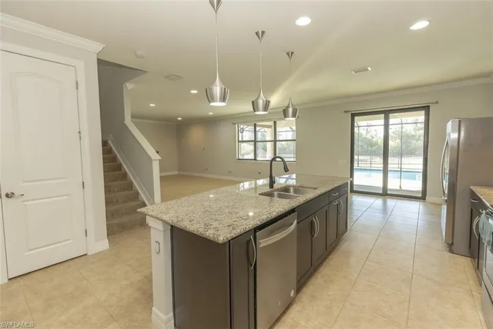 Kitchen with hanging light fixtures, a kitchen island with sink, stainless steel appliances, light tile patterned floors, and light stone counters