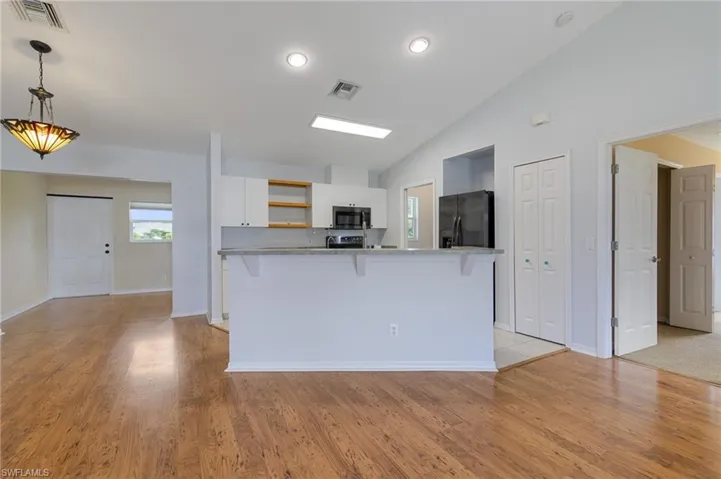 Kitchen featuring a breakfast bar area, white cabinets, light wood-style floors, open shelves, and high vaulted ceiling