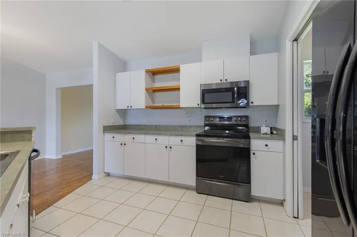 Kitchen featuring open shelves, range with electric stovetop, fridge with ice dispenser, stainless steel microwave, and white cabinets