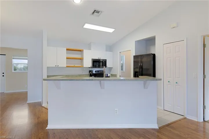 Kitchen with white cabinetry, light countertops, appliances with stainless steel finishes, open shelves, and light wood-type flooring