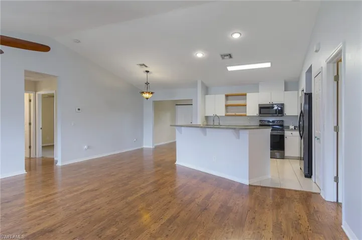 Kitchen featuring a breakfast bar, open shelves, white cabinets, electric range oven, and vaulted ceiling