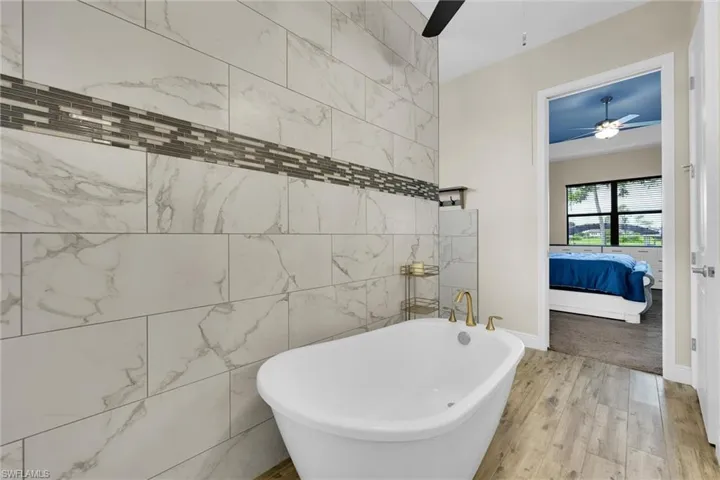 Primary bathroom with tasteful gold trim upgrades and finishes featuring a double vanity, a freestanding luxury soaking tub, extremely large separate walk-in shower, flooring throughout, and access to the deep walk-in closet