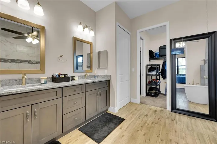 Primary bathroom with tasteful gold trim upgrades and finishes featuring a double vanity, a freestanding luxury soaking tub, extremely large separate walk-in shower, flooring throughout, and access to the deep walk-in closet