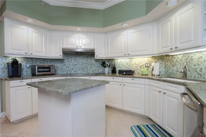 Kitchen with tasteful backsplash, dishwasher, a kitchen island, light tile floors, and white cabinets