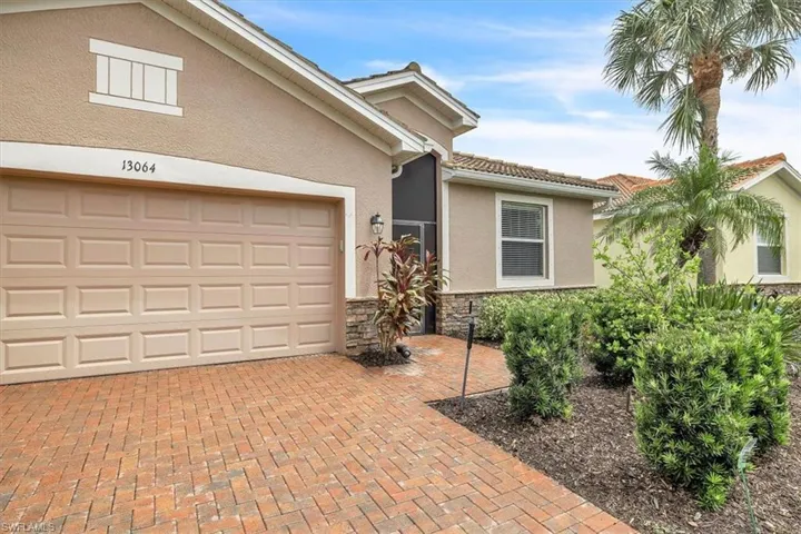 Paver driveway and walkway, stucco exterior with stacked stone accents, decorative garage door, and lush landscaping