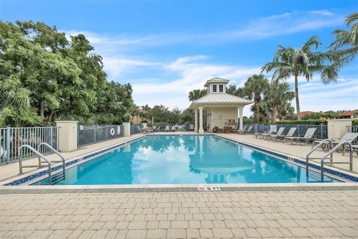 Rectangular swimming pool with a tiled perimeter, paver decking, surrounding safety fencing, and a permanent poolside cabana structure