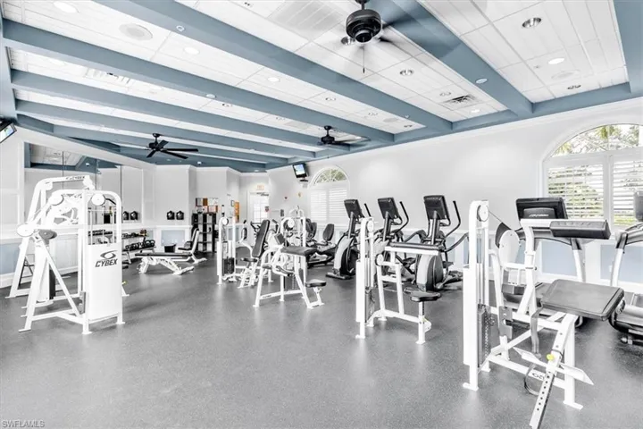 Fitness center featuring arched windows with plantation shutters, ceiling fans, and recessed lighting
