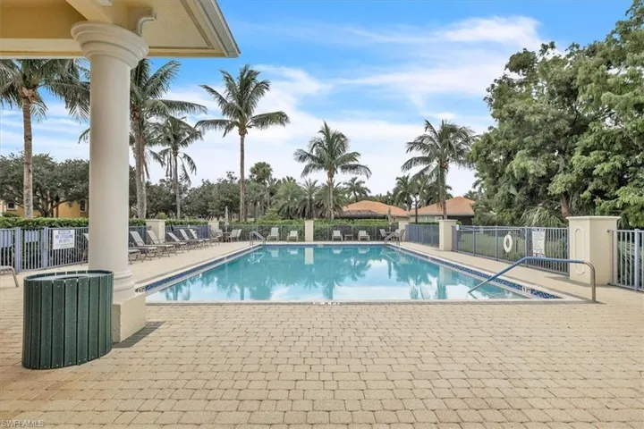 Outdoor swimming pool with a surrounding paved deck, fenced perimeter, and mature palm trees