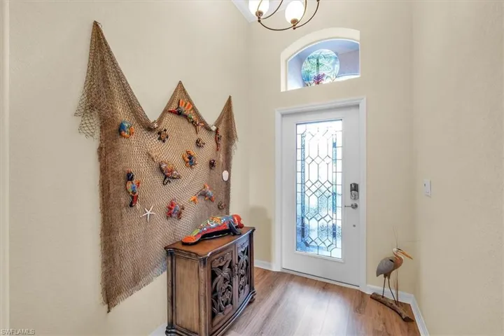 Wood-finish flooring, white entry door with decorative glass, arched transom window, and an overhead light fixture