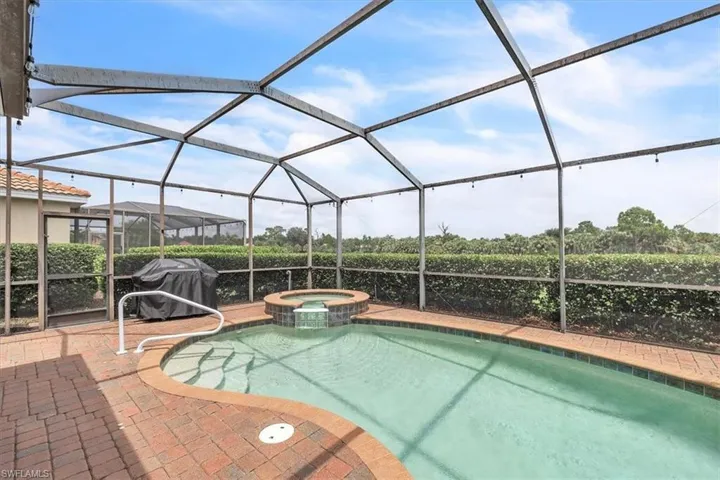 Screened-in outdoor living space featuring a swimming pool, integrated spa with waterfall, and brick paver decking