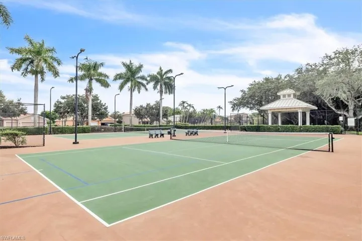 Tennis court with two playing surfaces, perimeter fencing, multiple light standards, and a nearby gazebo
