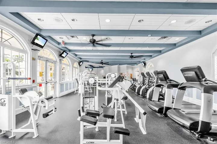 Fitness center featuring diverse exercise equipment, arched windows, exposed ceiling beams, ceiling fans, and integrated wall-mounted screens