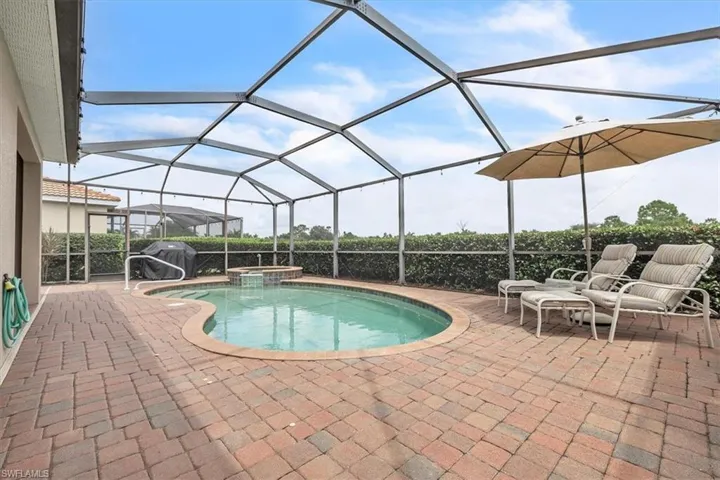 Screened-in pool area featuring a freeform swimming pool, integrated spa, and brick paver patio