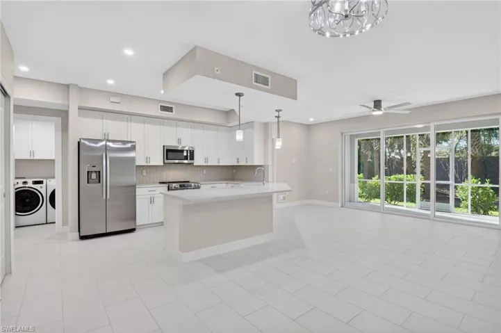 Kitchen featuring stainless steel appliances, white cabinetry, open floor plan, decorative backsplash, and a ceiling fan