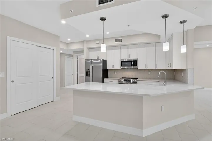 Kitchen featuring a peninsula, stainless steel appliances, white cabinets, tasteful backsplash, and decorative light fixtures