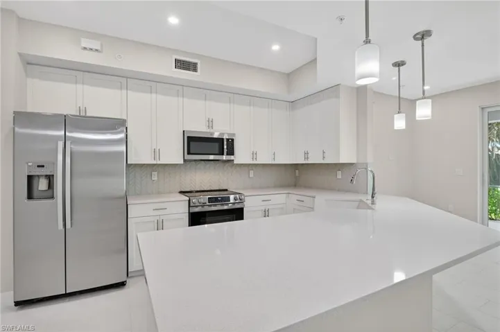 Kitchen with stainless steel appliances, a peninsula, pendant lighting, white cabinetry, and backsplash