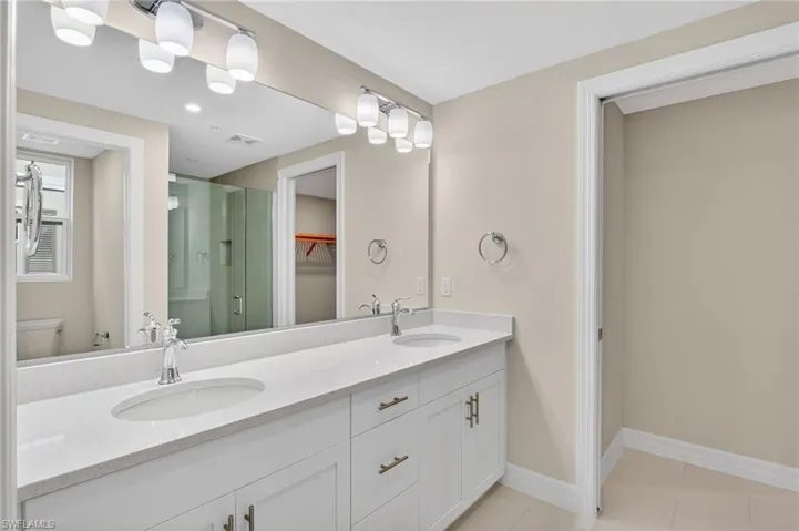 Full bath with double vanity, a shower stall, and light tile patterned floors