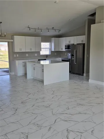 Kitchen with refrigerator, pendant lighting, range, lofted ceiling, and white cabinetry