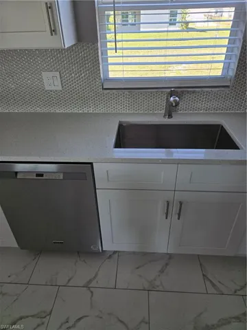 Kitchen featuring sink, decorative backsplash, white cabinetry, and dishwashing machine