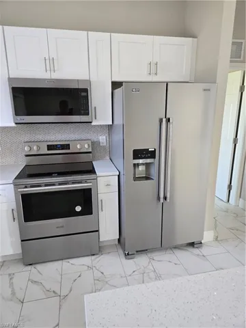 Kitchen featuring white cabinetry, fridge with ice dispenser, tasteful backsplash, and stove