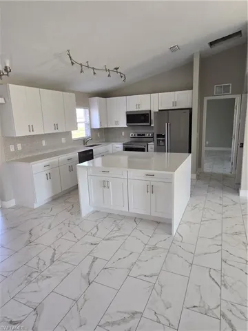 Kitchen with fridge, vaulted ceiling, stove, and white cabinetry