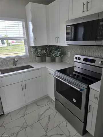 Kitchen featuring sink, white cabinets, decorative backsplash, and stainless steel range oven