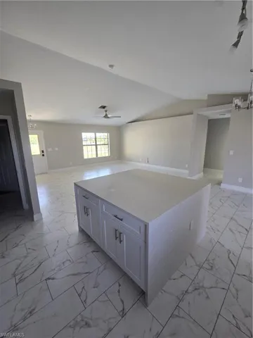 Kitchen featuring light stone countertops, a kitchen island, lofted ceiling, white cabinets, and ceiling fan