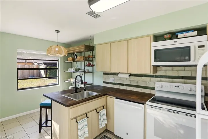 Kitchen featuring light wood finish cabinetry, white appliances, a peninsula, a breakfast bar, and pendant lighting