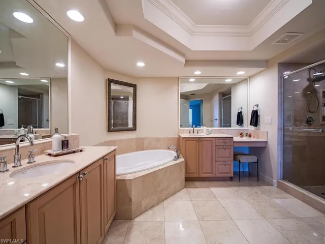 Bathroom with a raised ceiling, a stall shower, a garden tub, two vanities, and crown molding