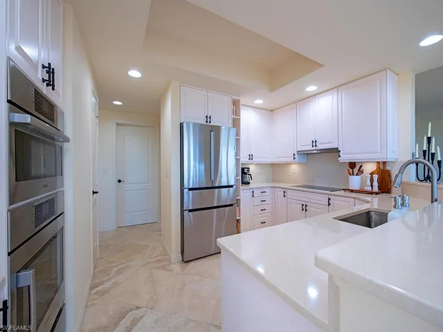 Kitchen with white cabinets, stainless steel appliances, open shelves, light stone counters, and recessed lighting