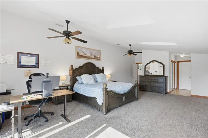 Bedroom featuring a skylight, lofted ceiling, carpet, a ceiling fan, and an office area