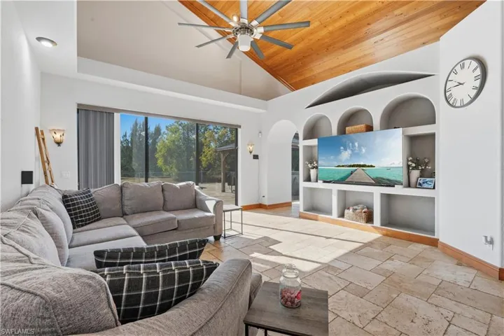Living room featuring stone tile floors, built in features, arched walkways, a ceiling fan, and high vaulted ceiling