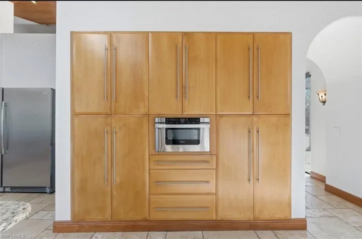 Kitchen with freestanding refrigerator, arched walkways, and stone tile floors